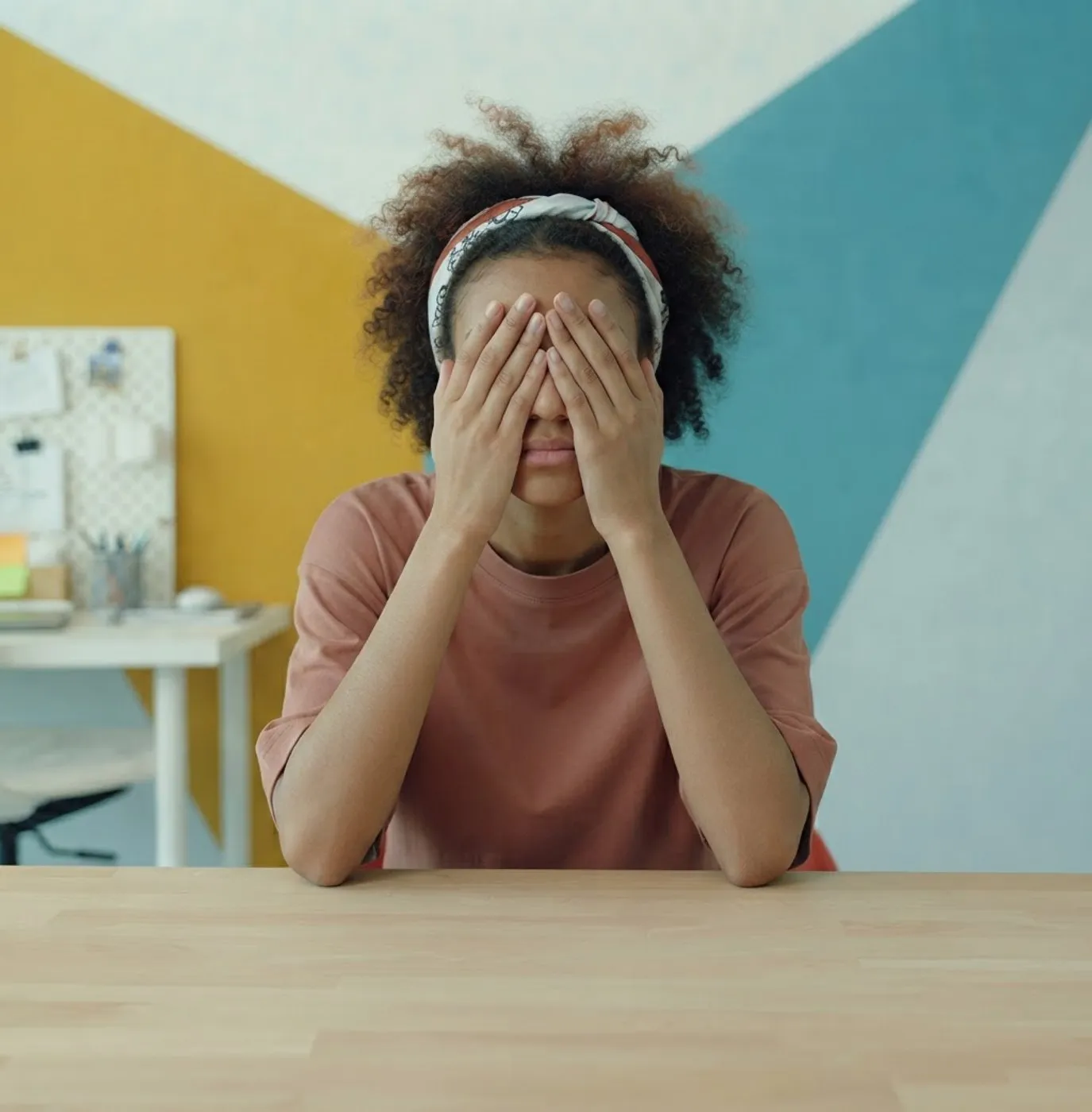 A woman sitting at a desk with both hands over her eyes